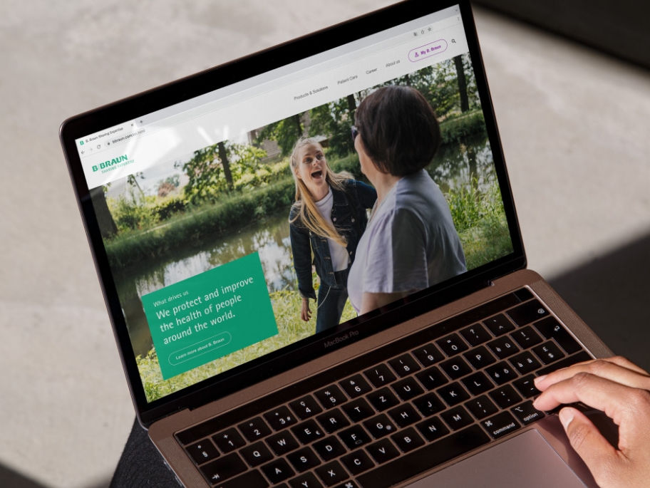 Một chiếc máy tính xách tay đang mở trang web của B. Braun, với một bàn tay đặt ở góc dưới bên phải của máy. 