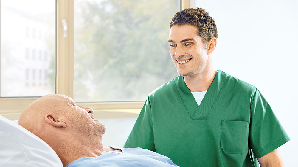 Y tá đang nói chuyện với bệnh nhân ở cạnh giường