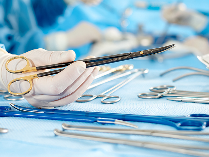 Nhiều dụng cụ phẫu thuật khác nhau trên bàn ở mặt trước một tay có kẹp kim màu đen